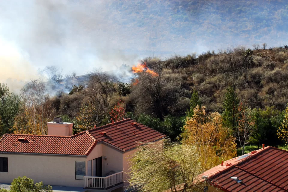 Wildfire approaching stucco house with red tile roof.